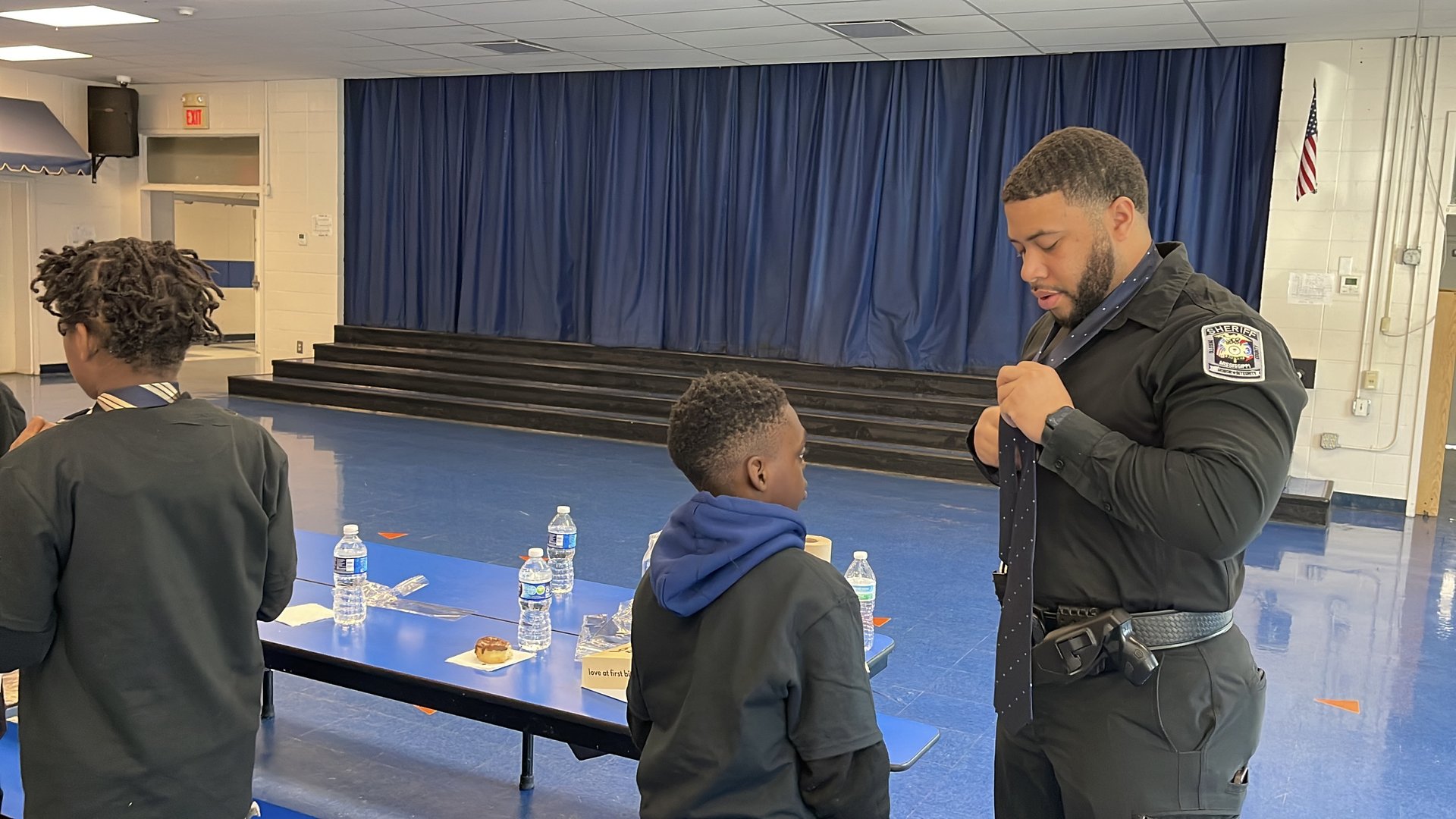 A DeSoto County School Resource Officer teaching students how to tie a necktie in the school cafeteria